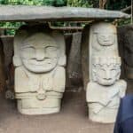 Visite d'une site archéologique avec statues en pierre, personne observant.