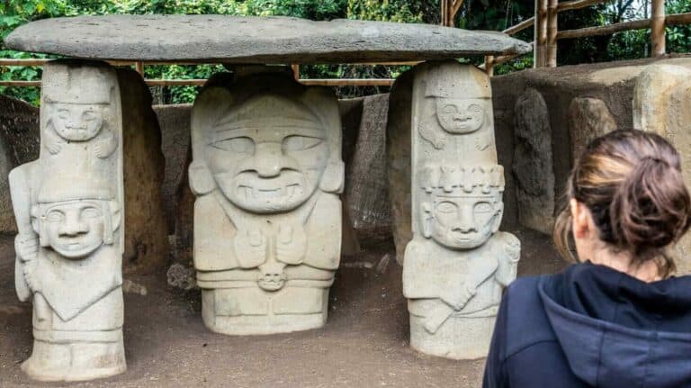 Visite d'une site archéologique avec statues en pierre, personne observant.