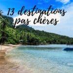 Plage avec arbres et bateau en eau calme, ciel bleu clair.