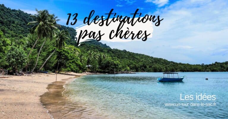 Plage avec arbres et bateau en eau calme, ciel bleu clair.