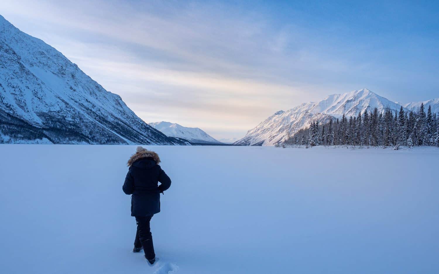 Personne regardant un lac gelé entouré de montagnes enneigées.