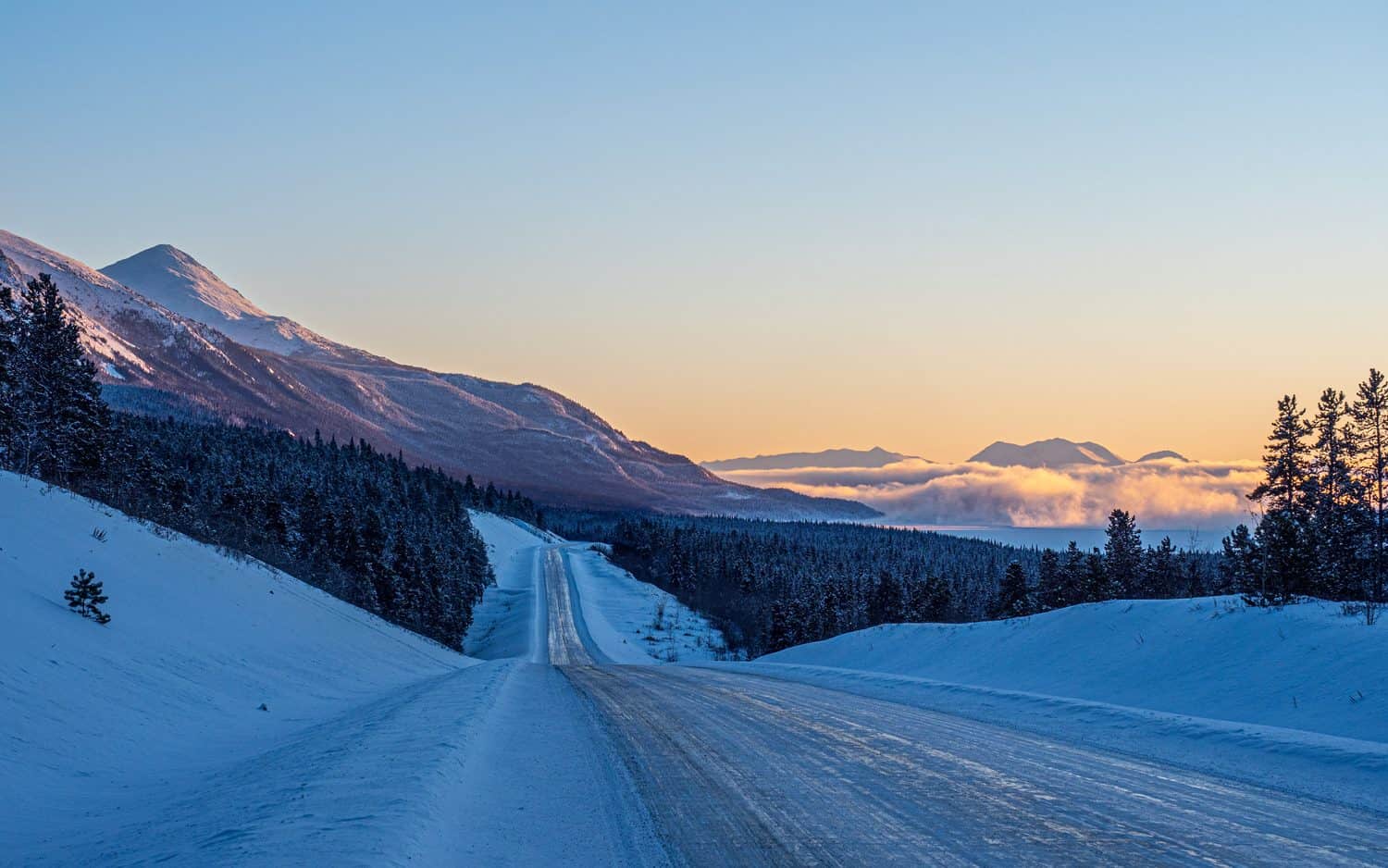Route enneigée dans un paysage de montagnes et de forêt au Yukon.