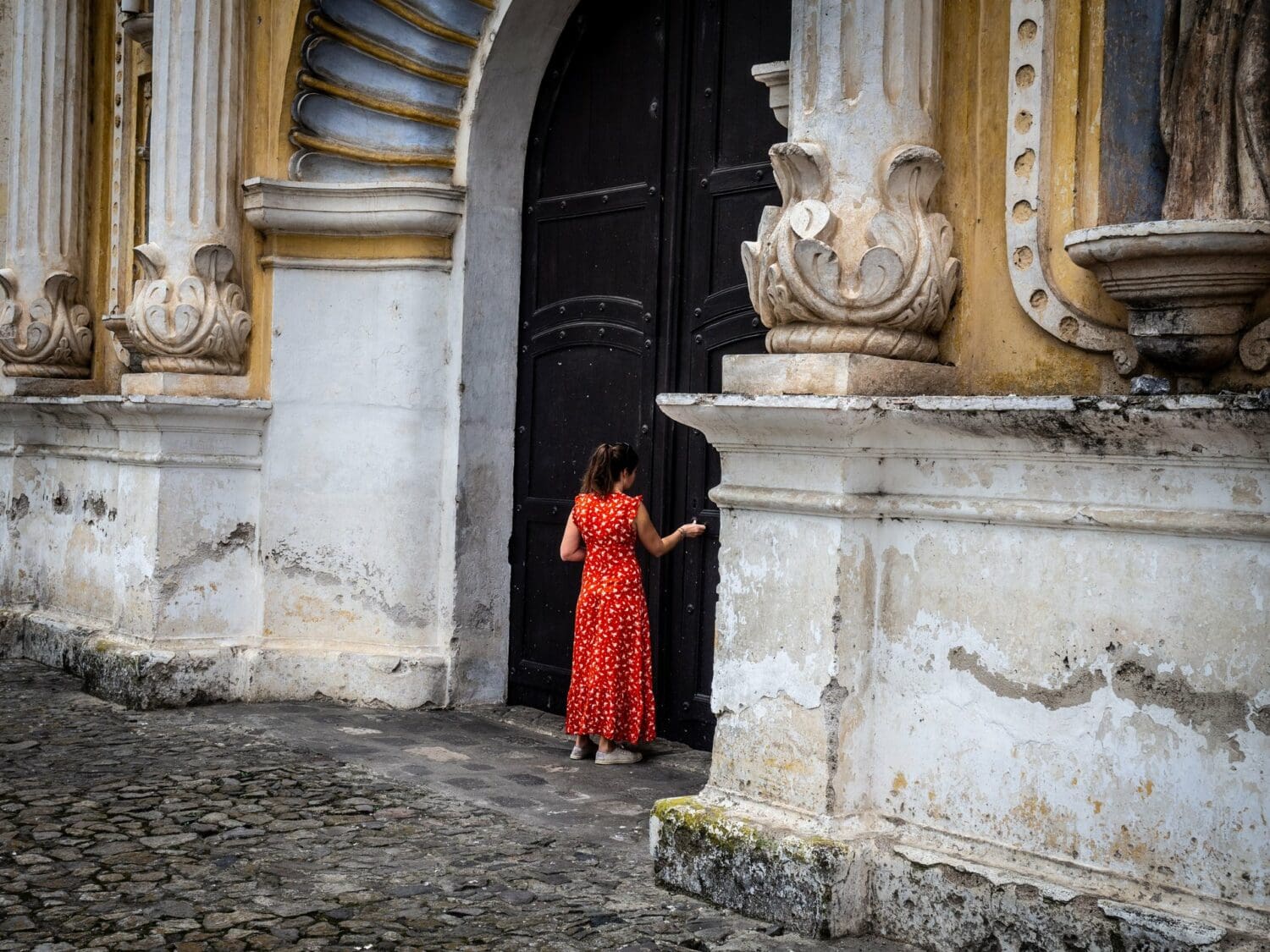 Femme en robe rouge devant la porte en bois de l’église de la Merced à Antigua