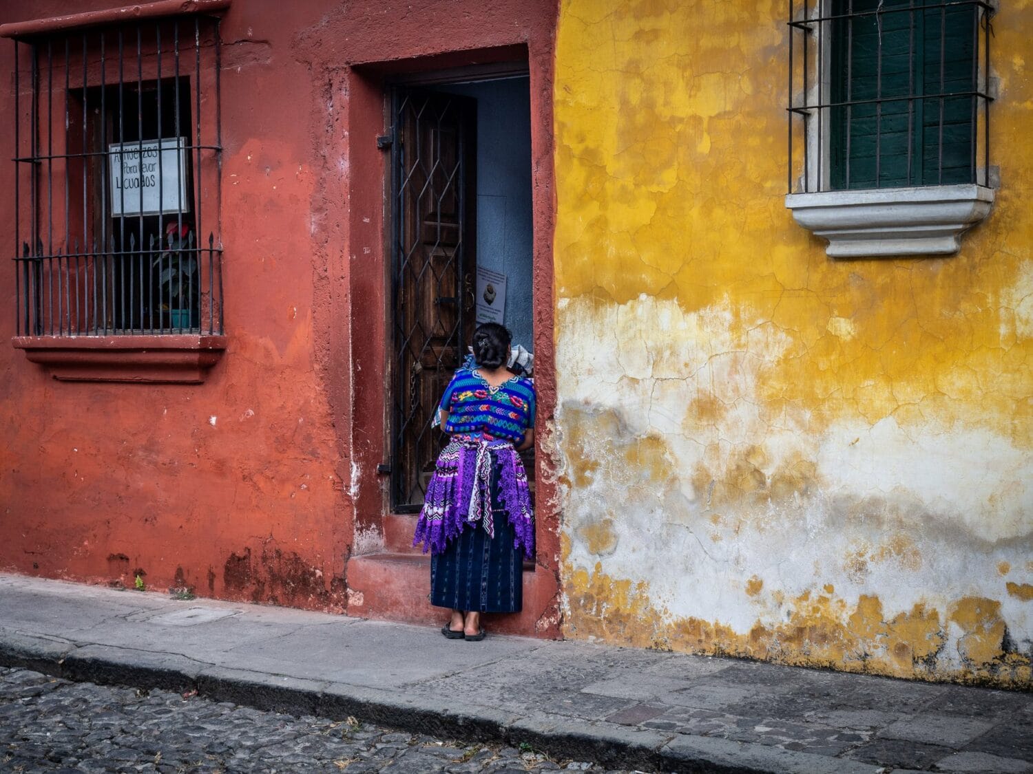 Femme maya en huipil devant une porte dans une rue colorée d’Antigua