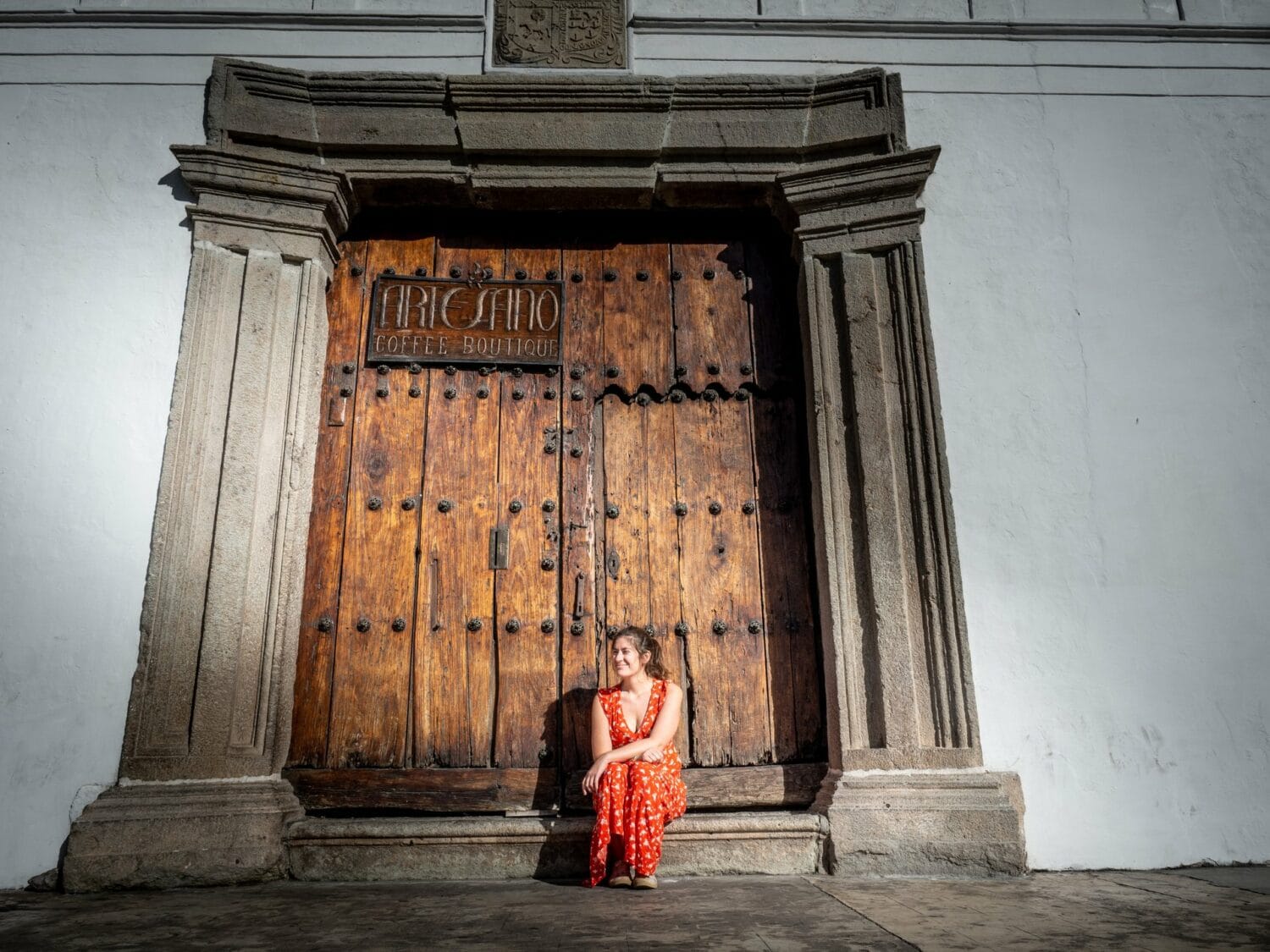 Femme assise devant la porte en bois d’un torréfacteur de café à Antigua